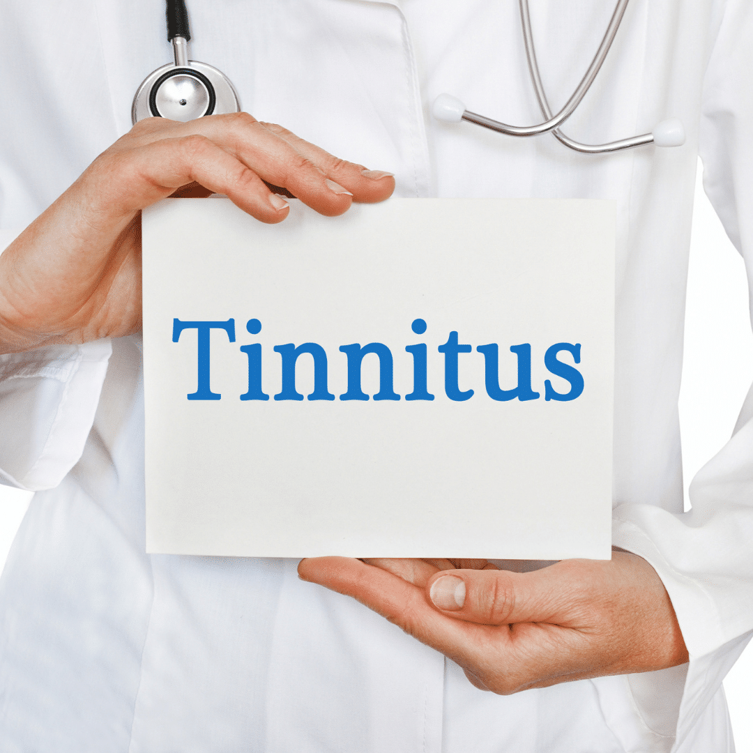 A person in a white lab coat wearing a stethoscope, holding a white sign that says "Tinnitus" in blue letters.   