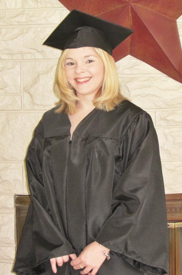 A white woman with blonde hair wearing a black graduation cap and robe.  