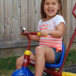 A Caucasian girl smiling while riding a tricycle.