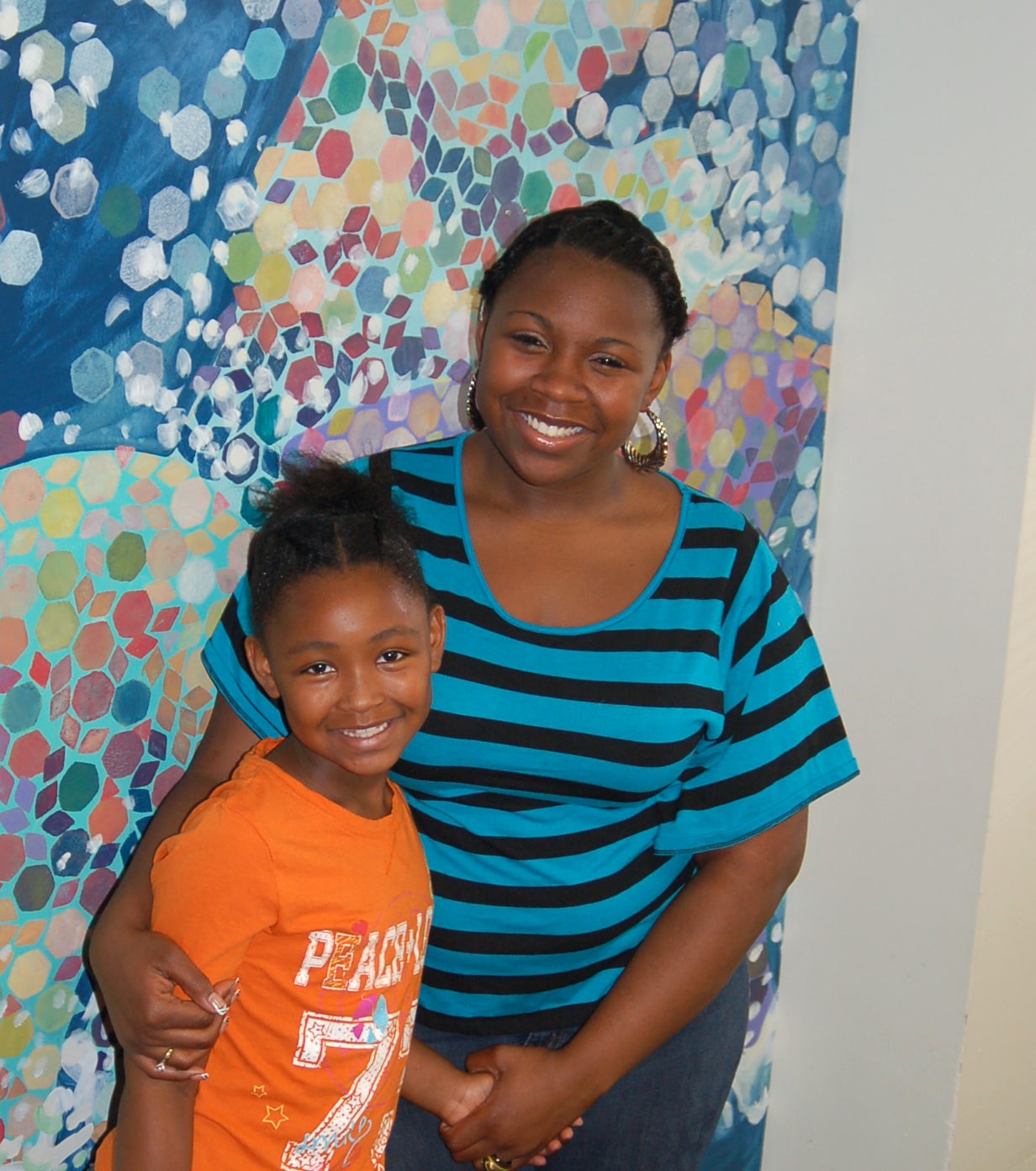 two young black ladies, the right wearing a black and blue striped top and the left is wearing an orange t-shirt.